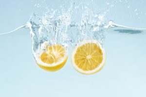 Citrus splash. Lemon halves splattering into clear water on blue background