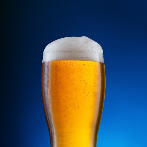 Glass with light beer on blue background